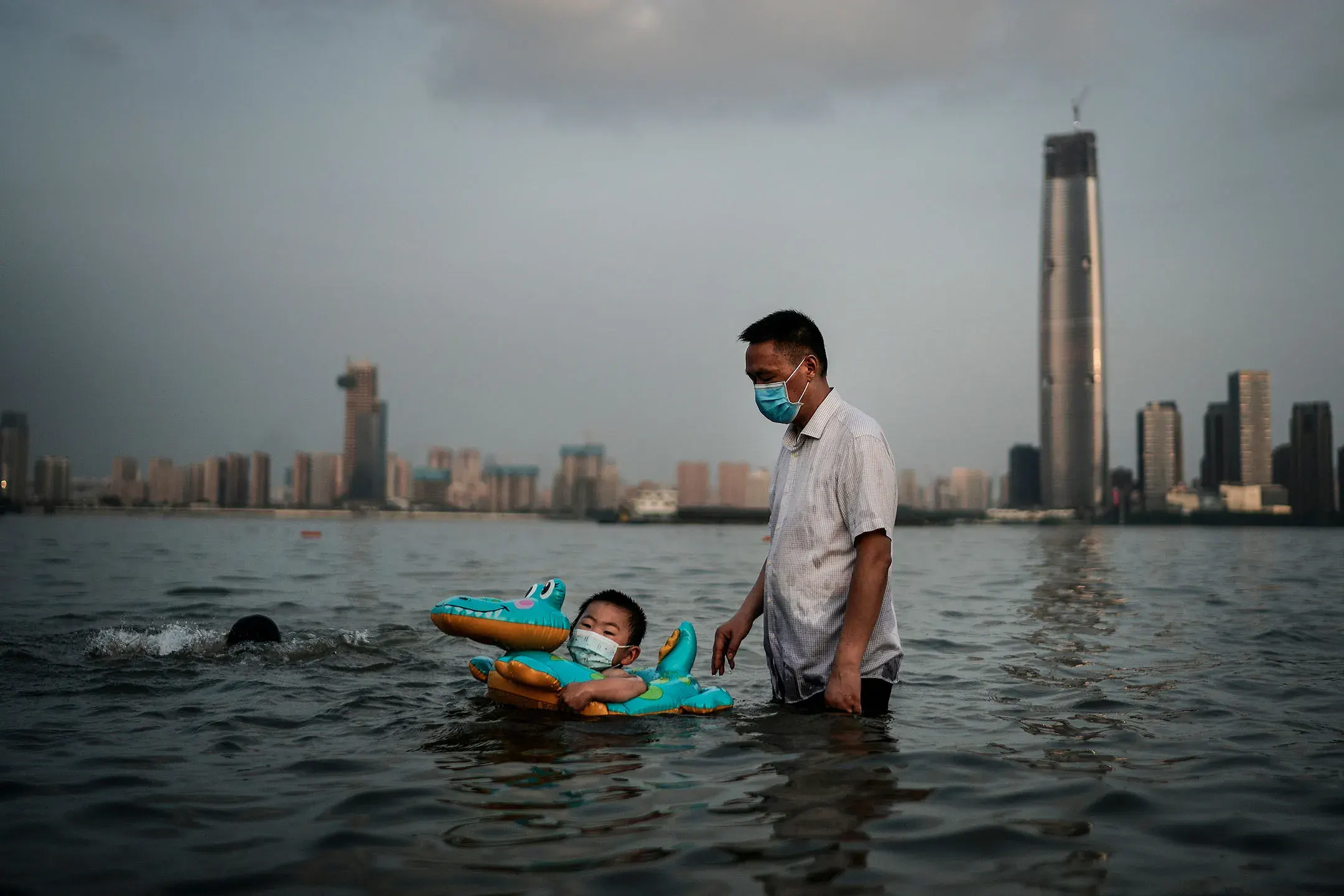 2020 年 6 月 30 日，中国武汉，一对父子在被洪水淹没的公园内，拿著橡胶圈游泳。摄：Getty Images
