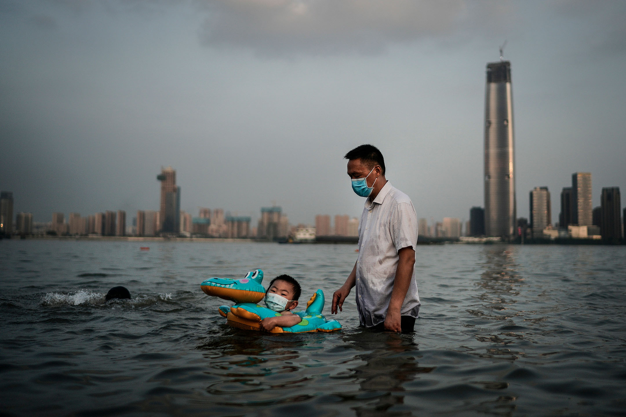2020年6月30日，中国武汉，一对父子在被洪水淹没的公园内，拿著橡胶圈游泳。摄：Getty Images